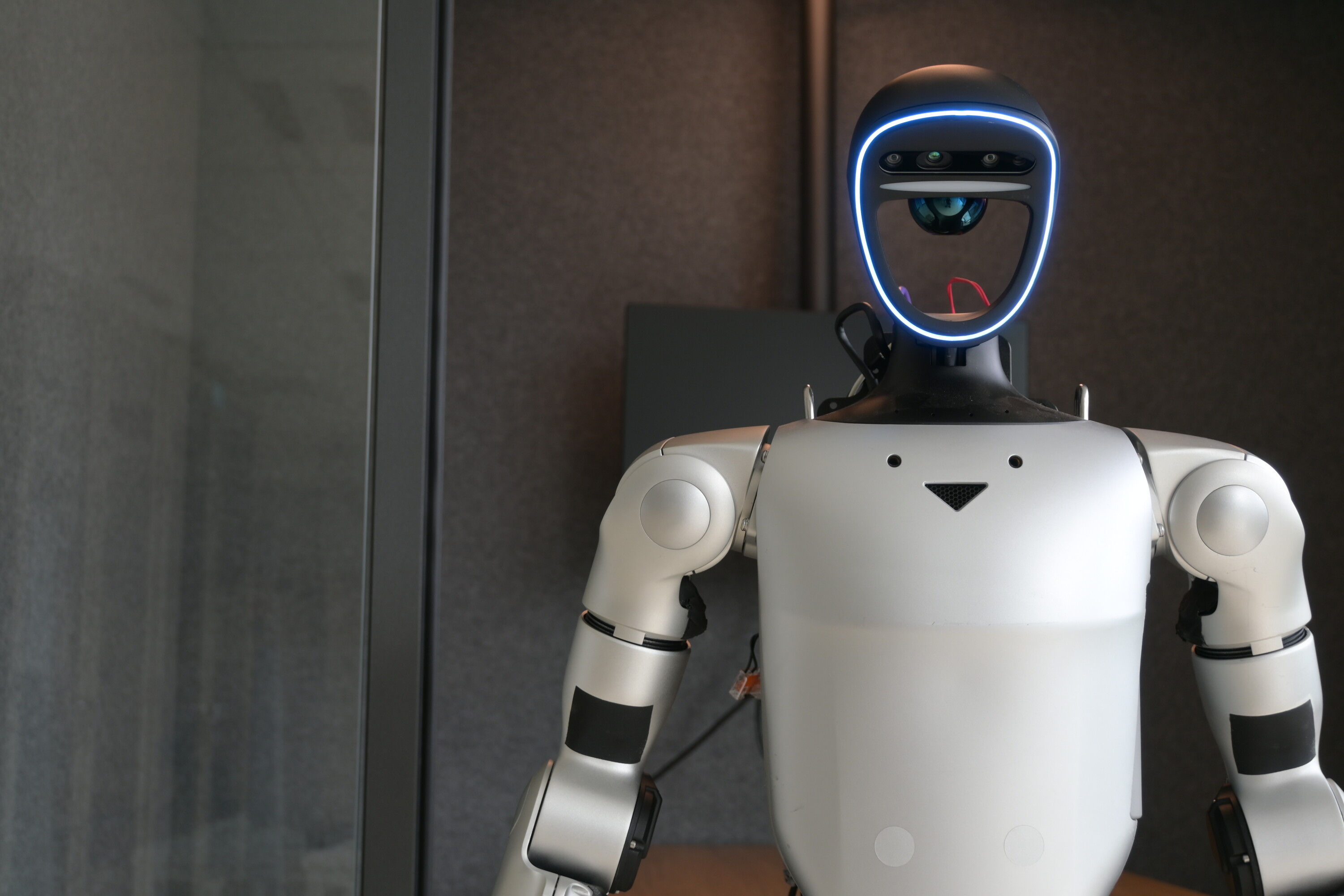 Unitree G1 humanoid facing the camera in a dark interior.